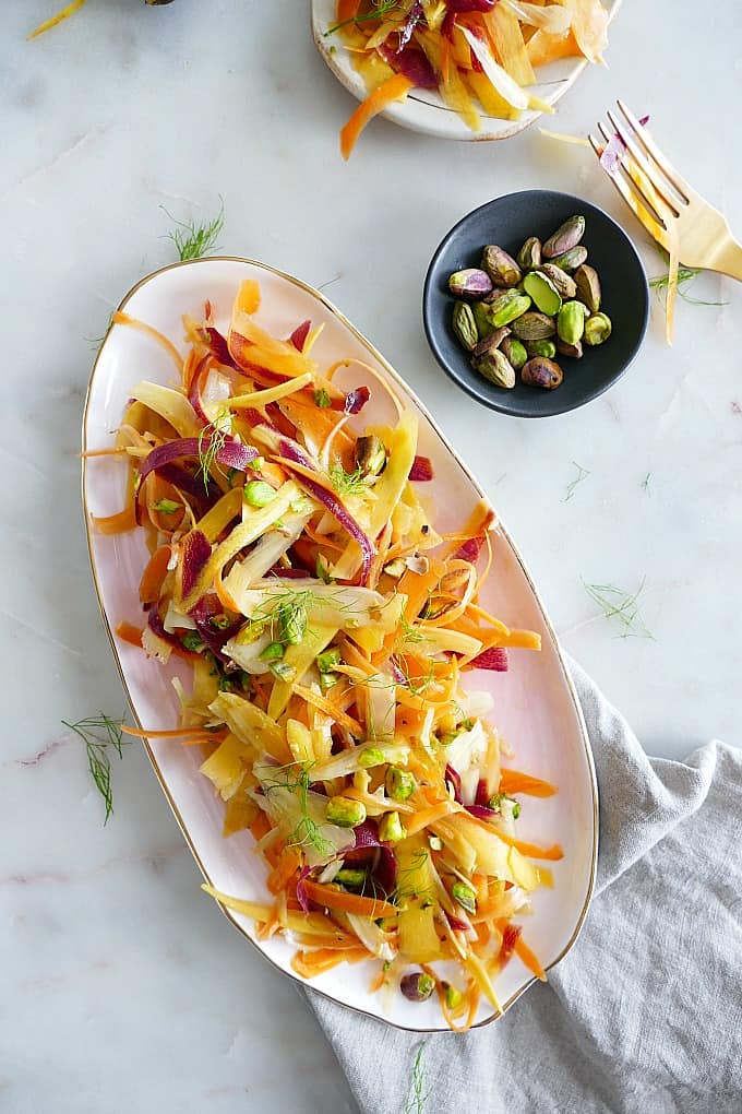 Shaved Carrot Fennel Salad on an oval platter next to pistachios and a fork