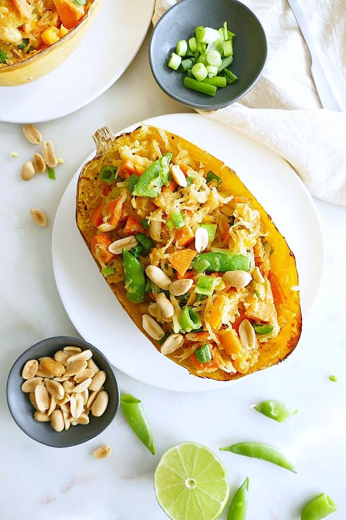 Spaghetti Squash Pad Thai on a white plate next to black bowls with toppings