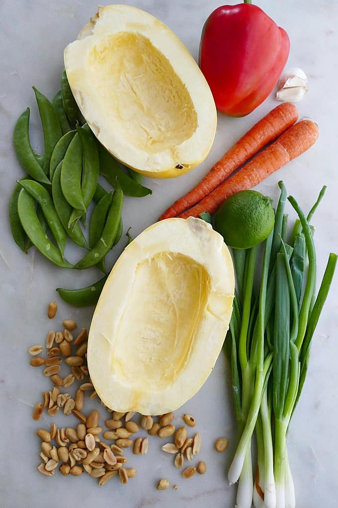 2 spaghetti squash halves, carrots, snap peas, scallions, peanuts, and pepper on counter