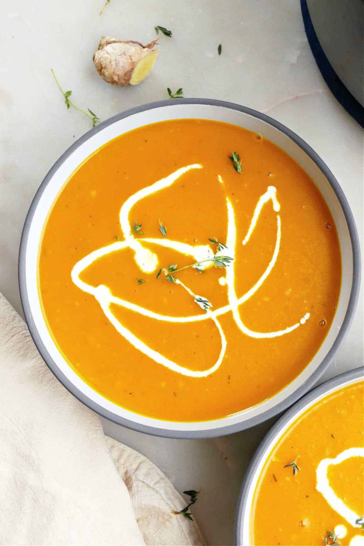 two bowls of soup topped with pumpkin seeds and thyme on a counter