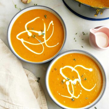 two bowls of kabocha squash soup next to soup pot with ladle