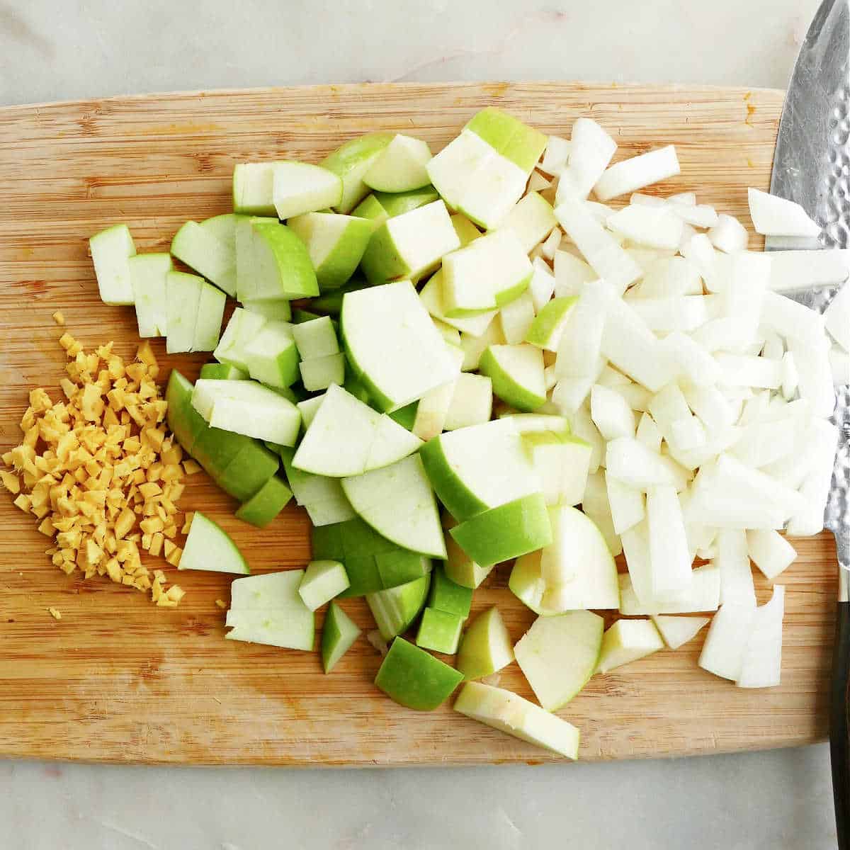 ginger, green apples, and onion diced into pieces on a cutting board