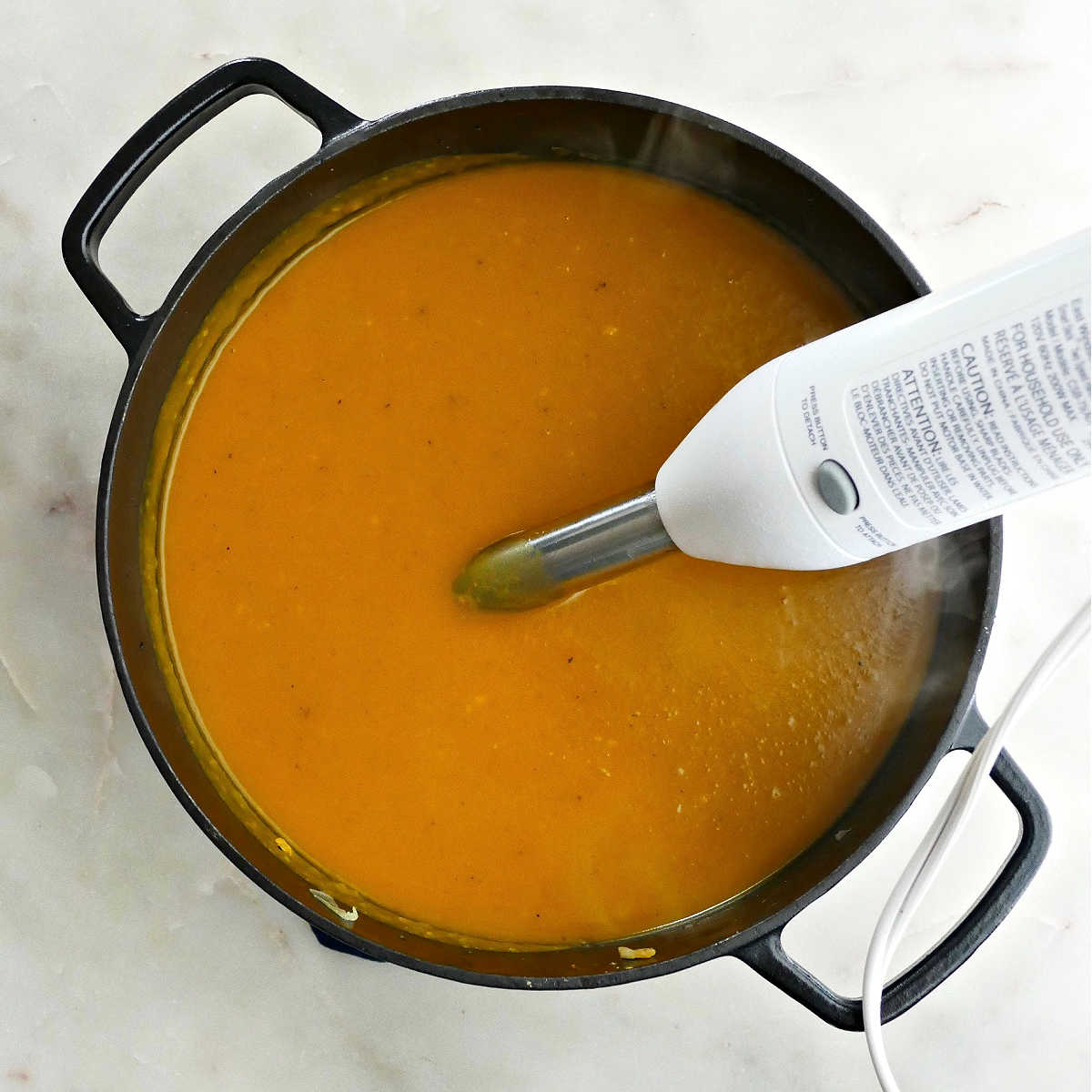 kabocha squash soup being blended with an immersion blender in a soup pot