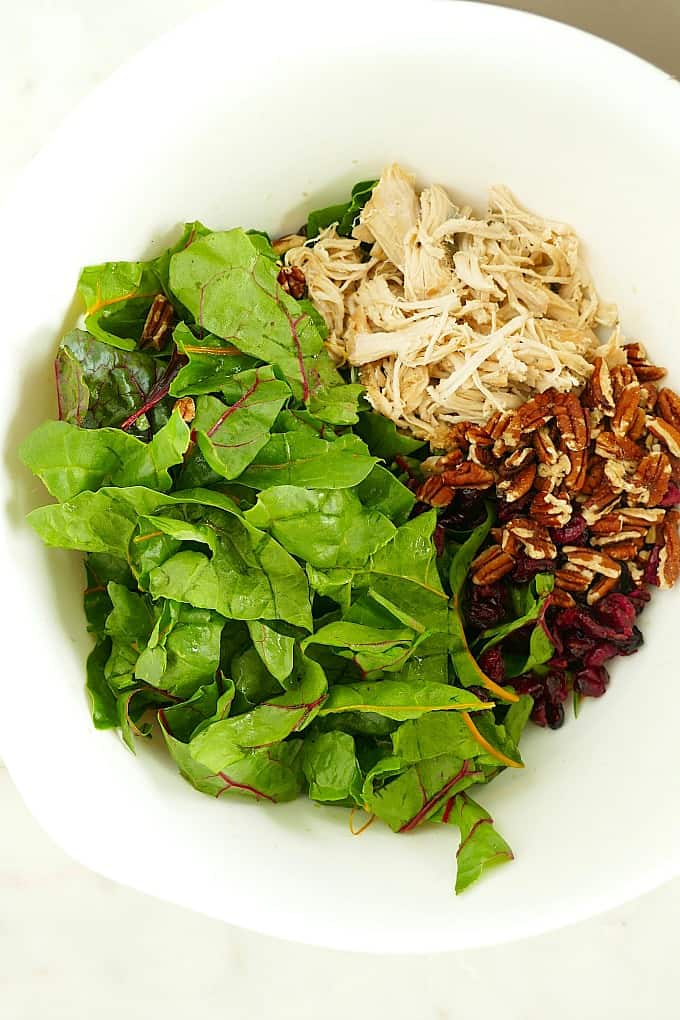 torn swiss chard, shredded turkey, pecans, and dried cranberries in a white mixing bowl