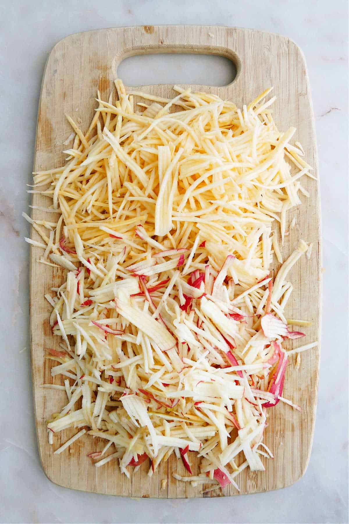 julienned rutabaga and apples on a bamboo cutting board on a counter