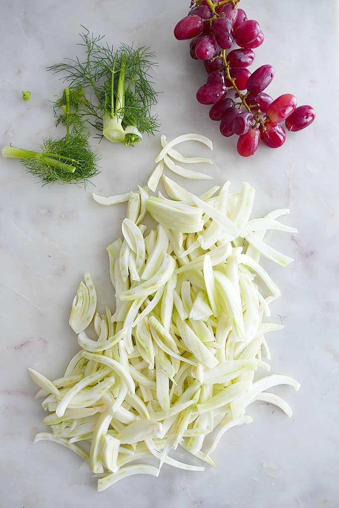 sliced fennel and fronds and red grapes on a white counter