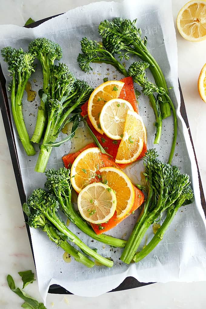 raw salmon fillets with orange glaze in between broccolini on a sheet pan