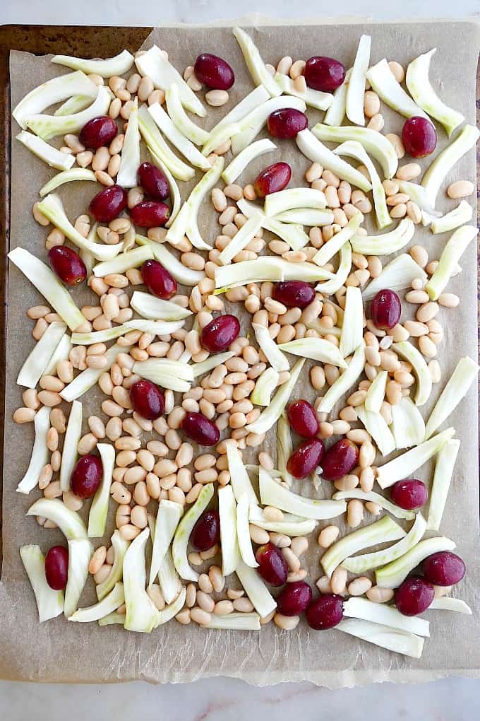 sliced fennel, white beans, and grapes on parchment paper on a baking sheet