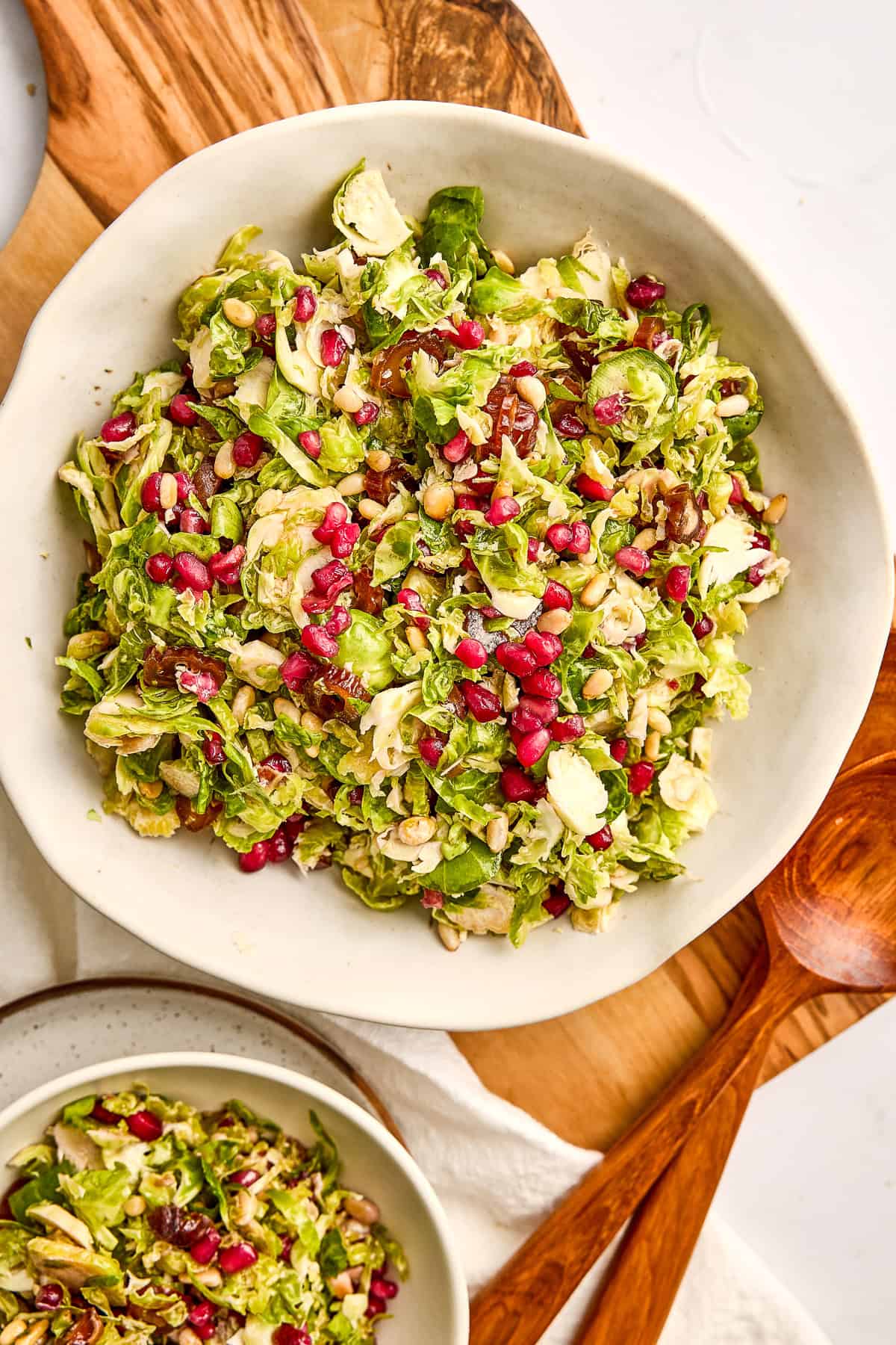 Brussels sprouts salad in a bowl on a wooden board next to servers.