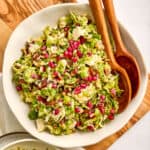 Brussels sprouts and date salad in a bowl with salad tongs on a wooden board.