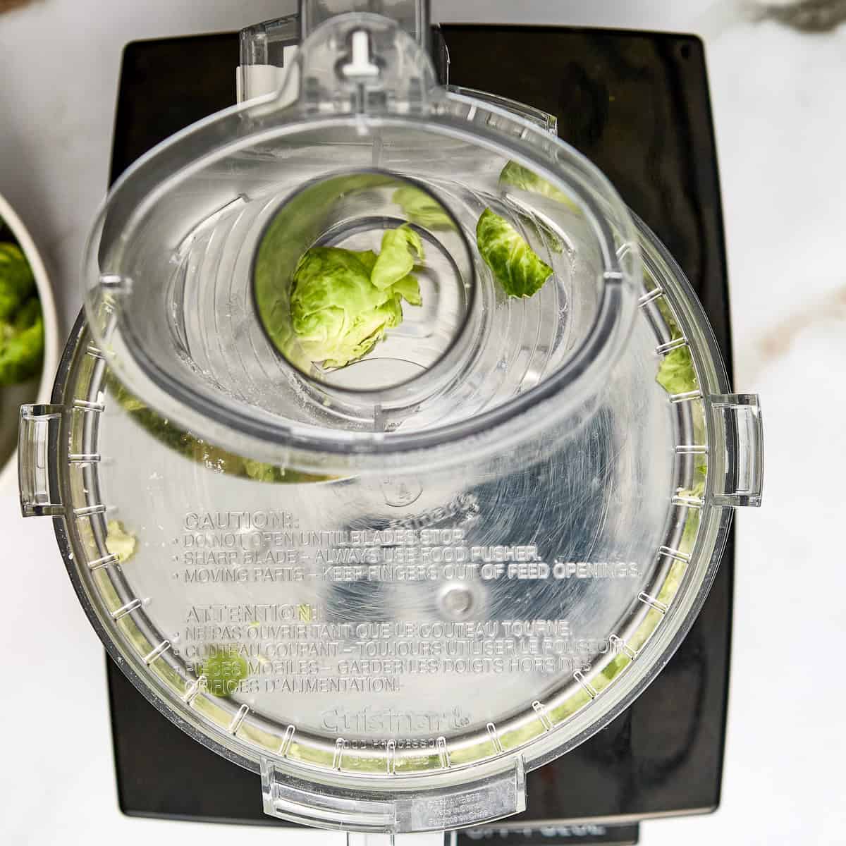Brussels sprouts being shred in a food processor with the slicing disk.