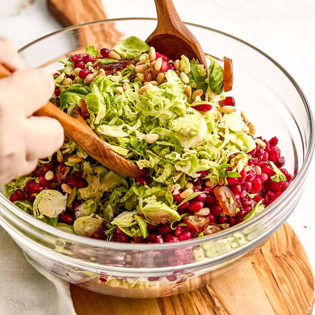 Woman mixing shaved Brussels sprouts, sliced dates, pomegranate arils, and pine nuts in a bowl.