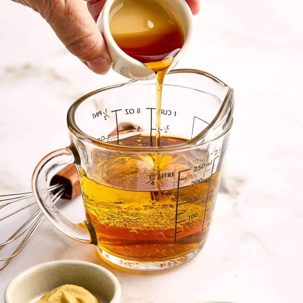 Woman pouring red wine vinegar into olive oil in glass measuring cup.