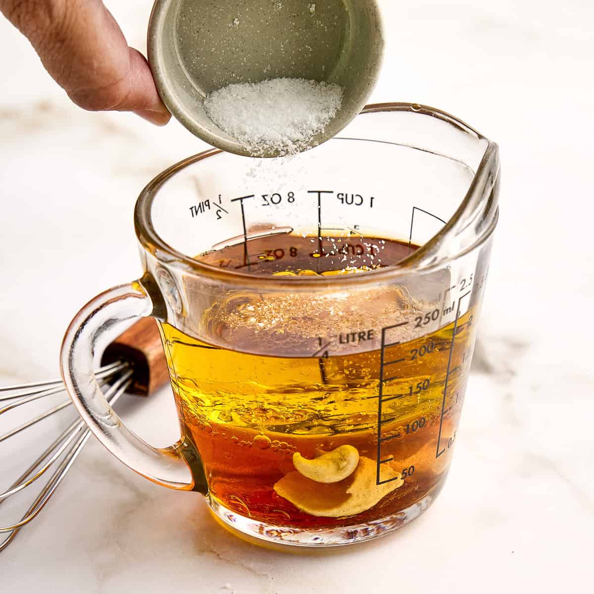 Woman sprinkling salt into oil and vinegar in a glass measuring cup.