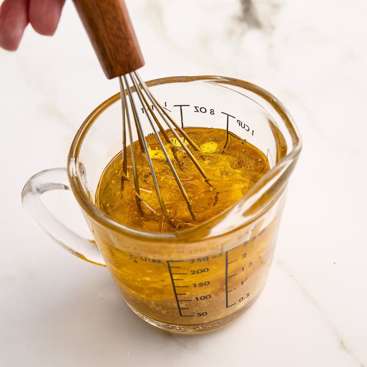 Woman mixing salad dressing ingredients with a whisk in a glass measuring cup.