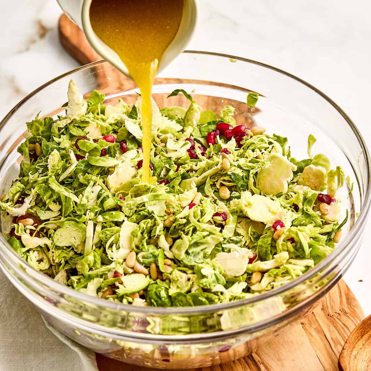 Woman pouring apple cider vinaigrette onto Brussels sprouts salad in a bowl.