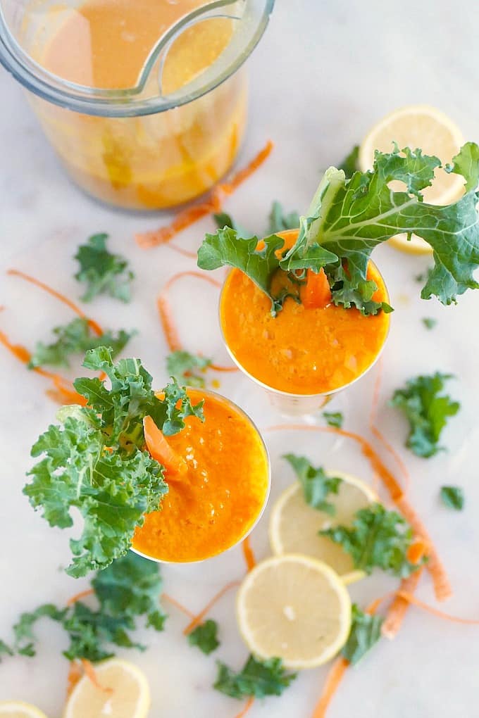 overhead shot of two carrot juice cocktails garnished with kale leaves and carrot sticks
