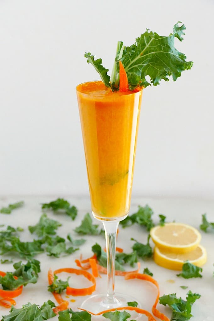 champagne flute with a fresh mimosa garnished with a kale leaf and carrot stick
