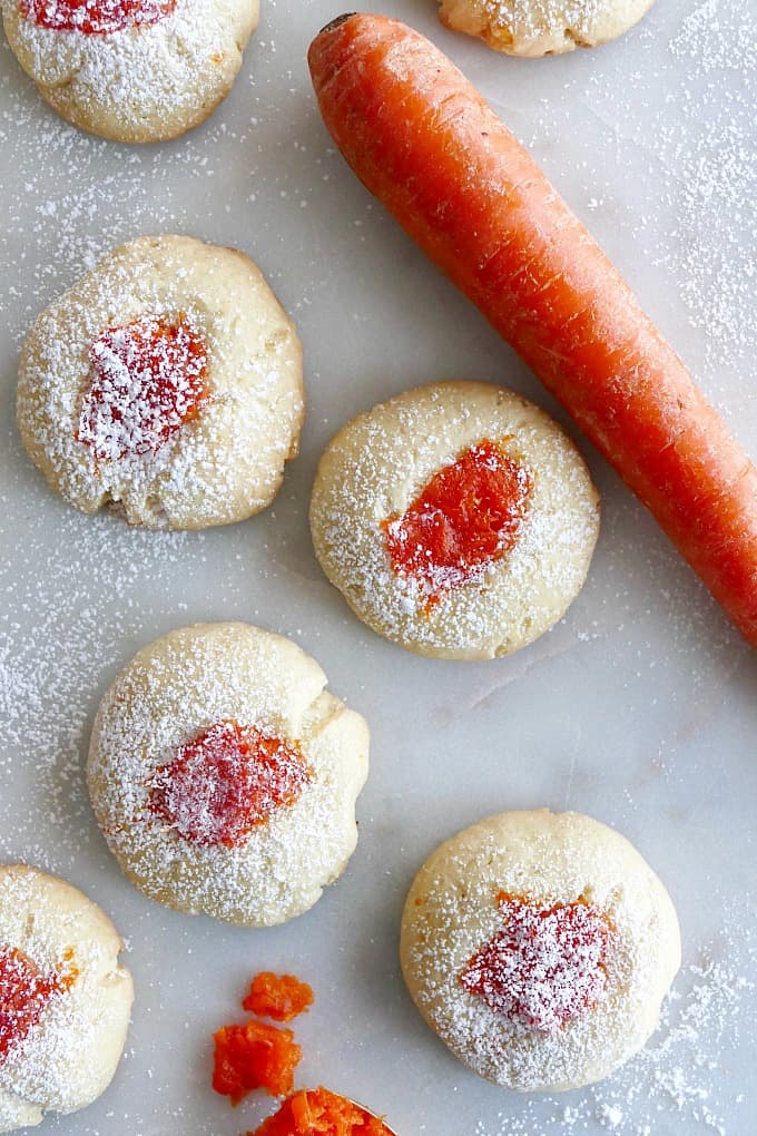 four thumbprint cookies with carrot jam on white counter with large carrot