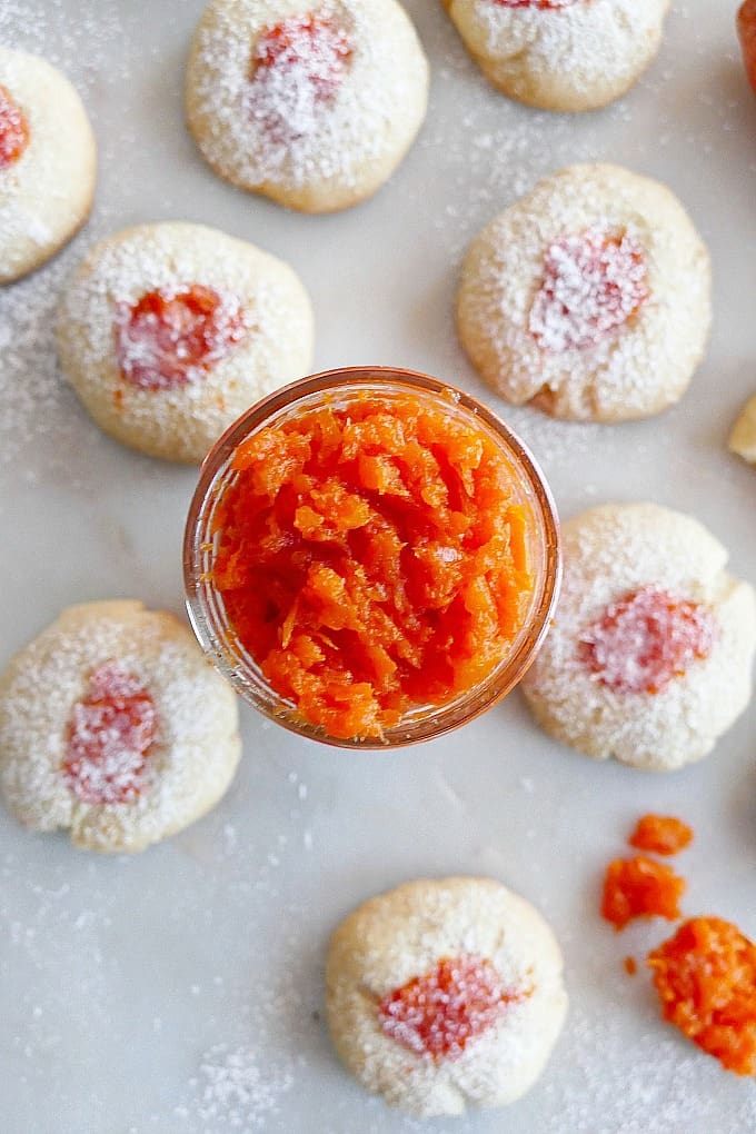 jar of carrot jam in the middle of thumbprint cookies on white countertop