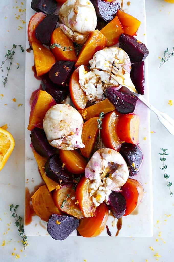 sliced golden and red roasted beets on a white cheese board with burrata and dressing