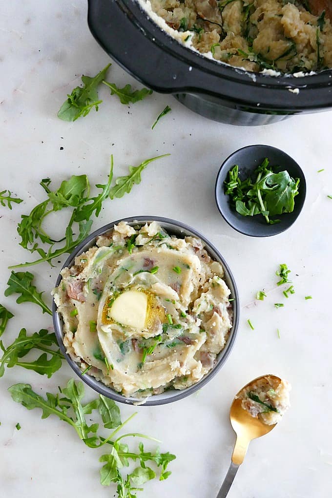 blue bowl with mashed potatoes next to arugula, crockpot, and small bowl