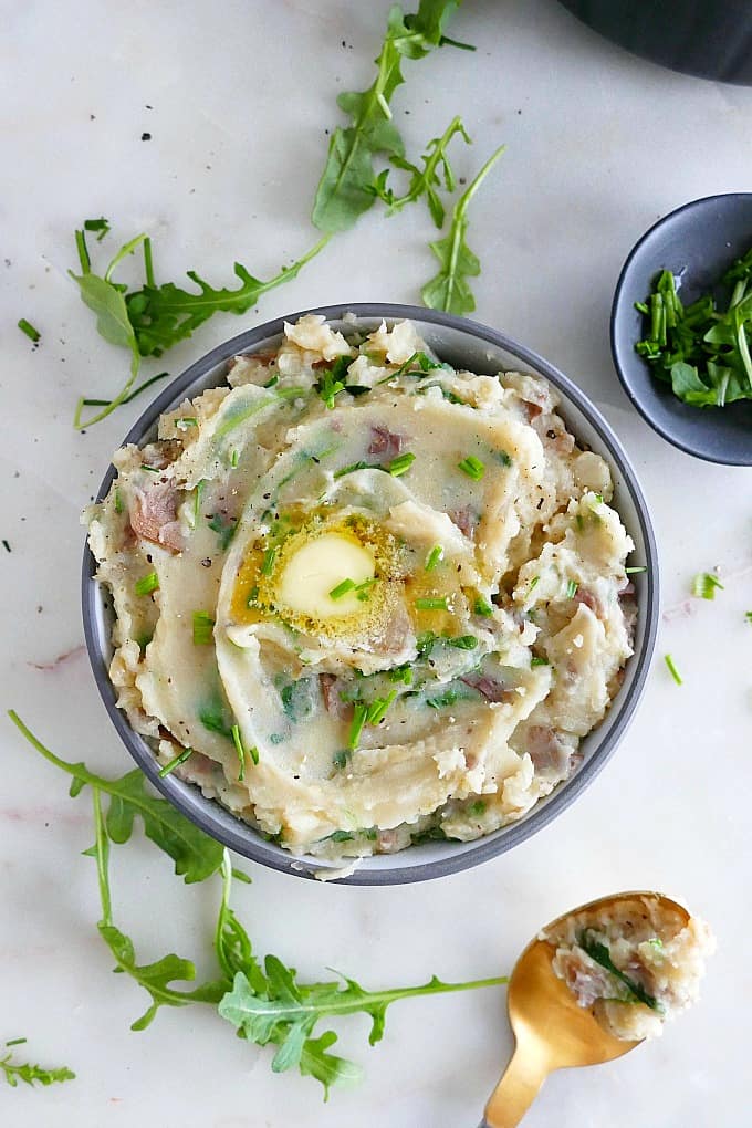 grey bowl with mashed potatoes, chives, and butter on a counter