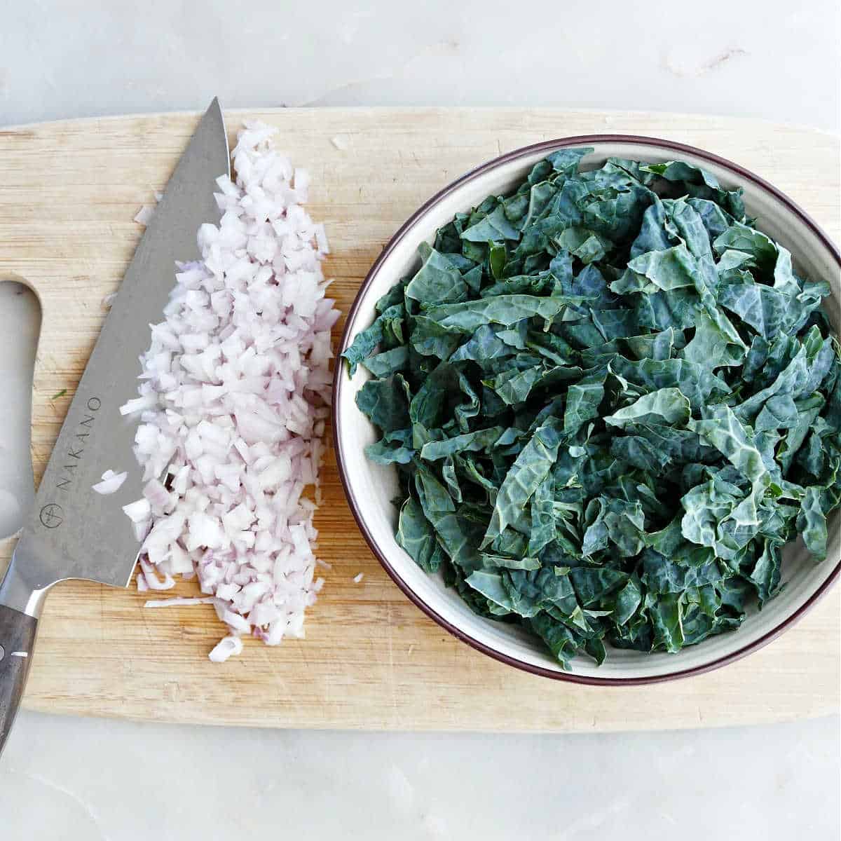 diced shallots and chopped kale on a cutting board next to chef's knife