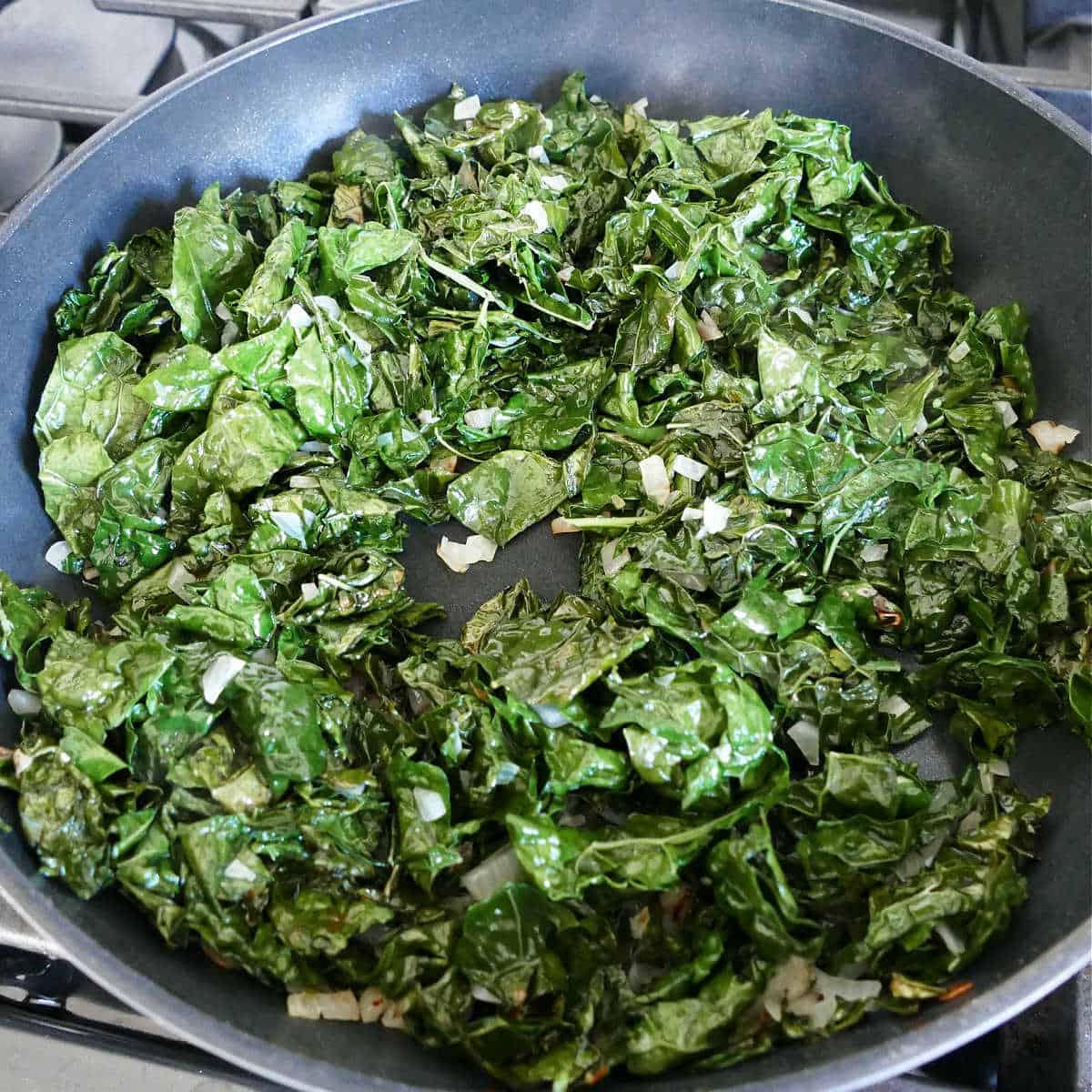 kale and shallots cooking in olive oil in a skillet on a stove