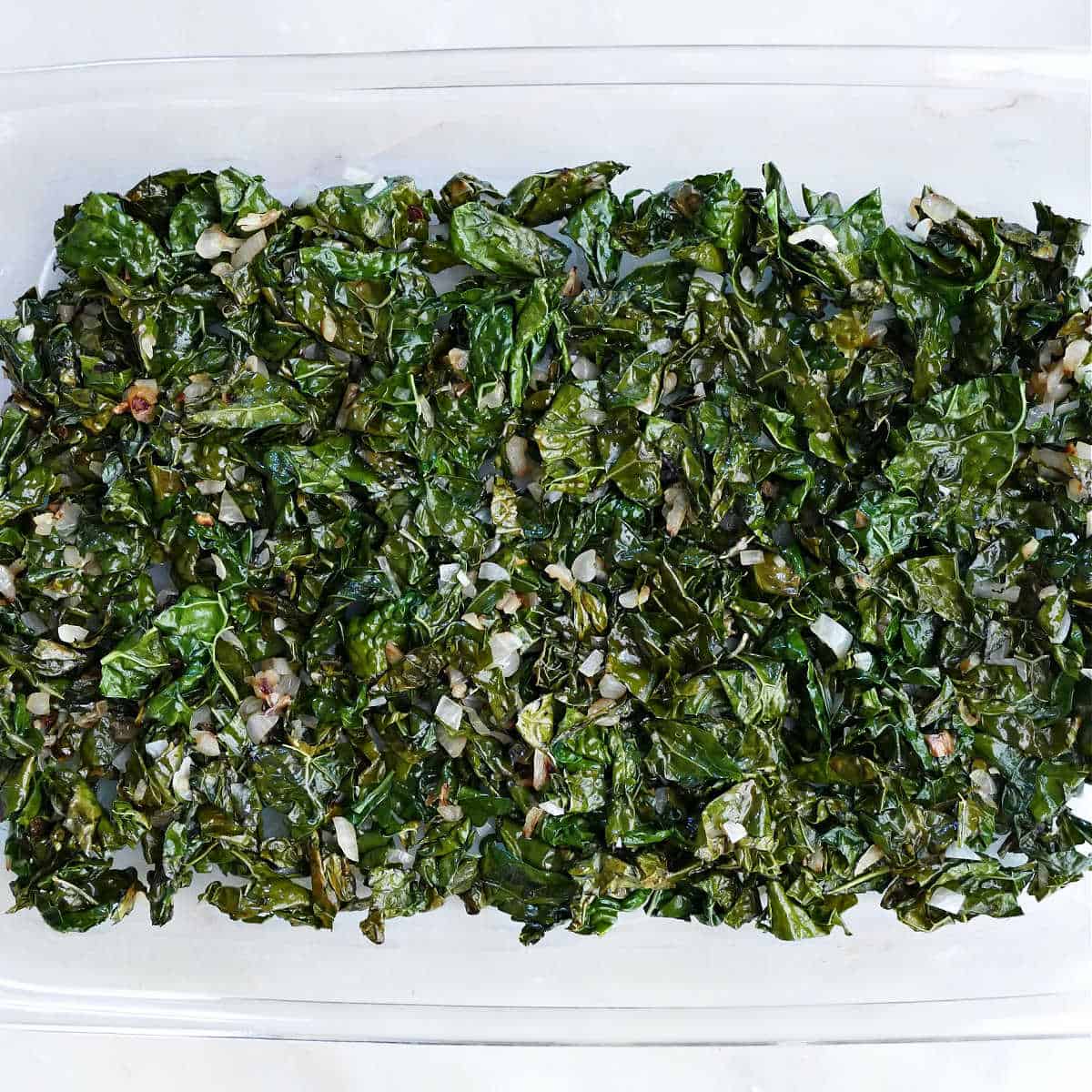 cooked kale and shallots in the bottom of a baking dish