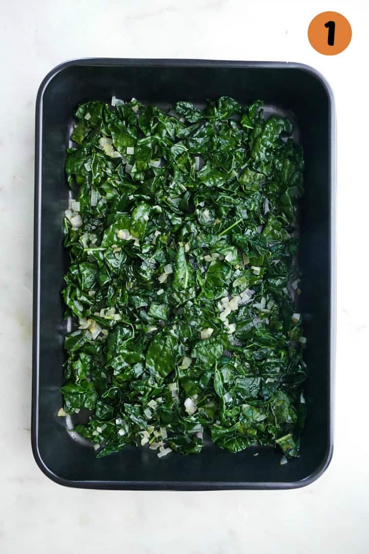 sauteed kale and shallots in a black 9x13 baking dish on a counter