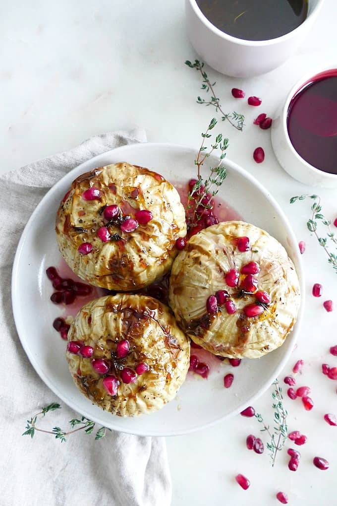 three whole roasted kohlrabis with pomegranate seeds on a white plate on a counter