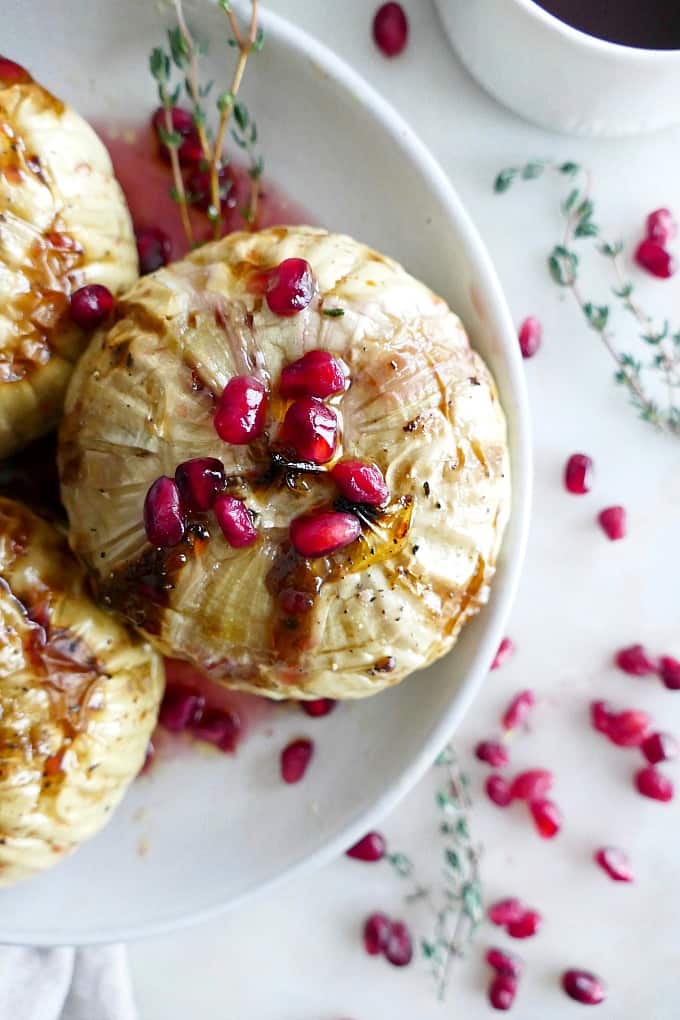 close up of one whole roasted kohlrabi with pomegranate seeds on a white plate