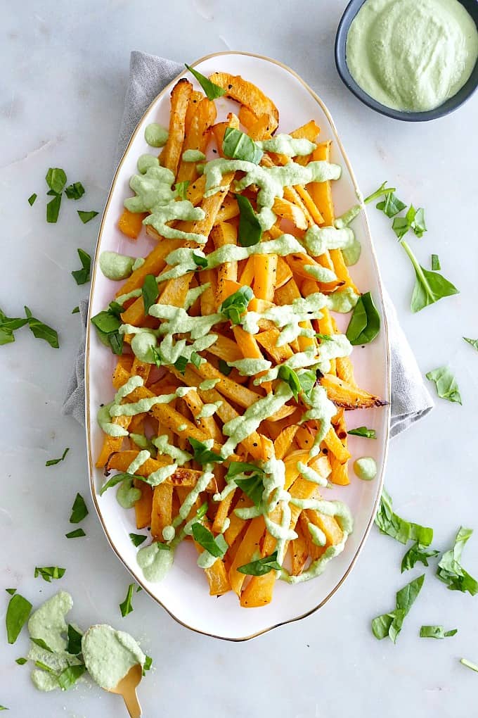 rutabaga fries on an oval serving tray drizzled with spinach cashew cream on a counter