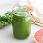 grapefruit, kale, and banana smoothie in a glass with grapefruit wedge on the rim