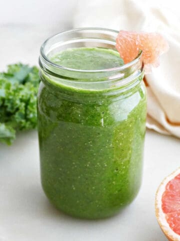 grapefruit, kale, and banana smoothie in a glass with grapefruit wedge on the rim