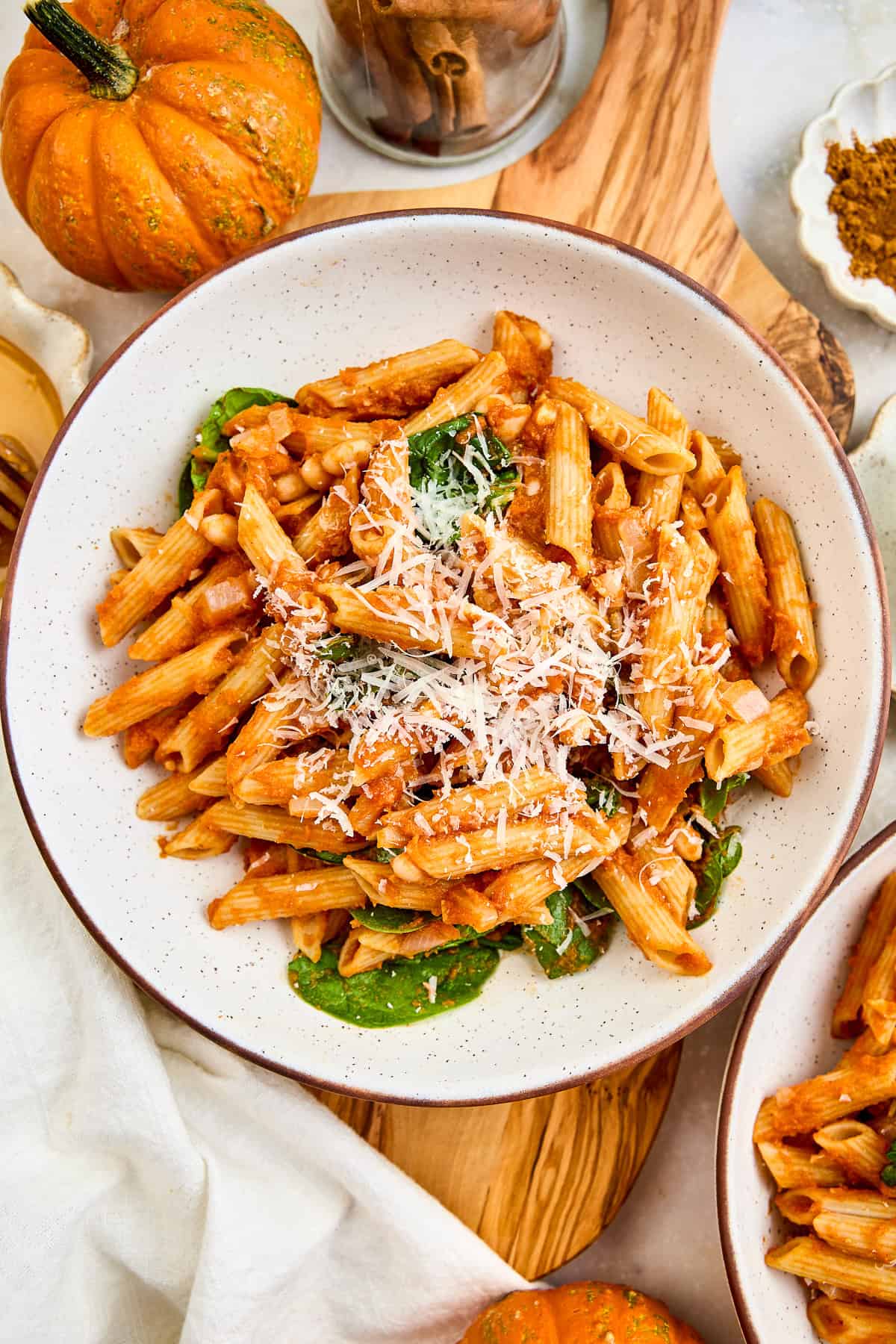 Pumpkin pasta in a bowl on a board next to a pumpkin and ingredients.