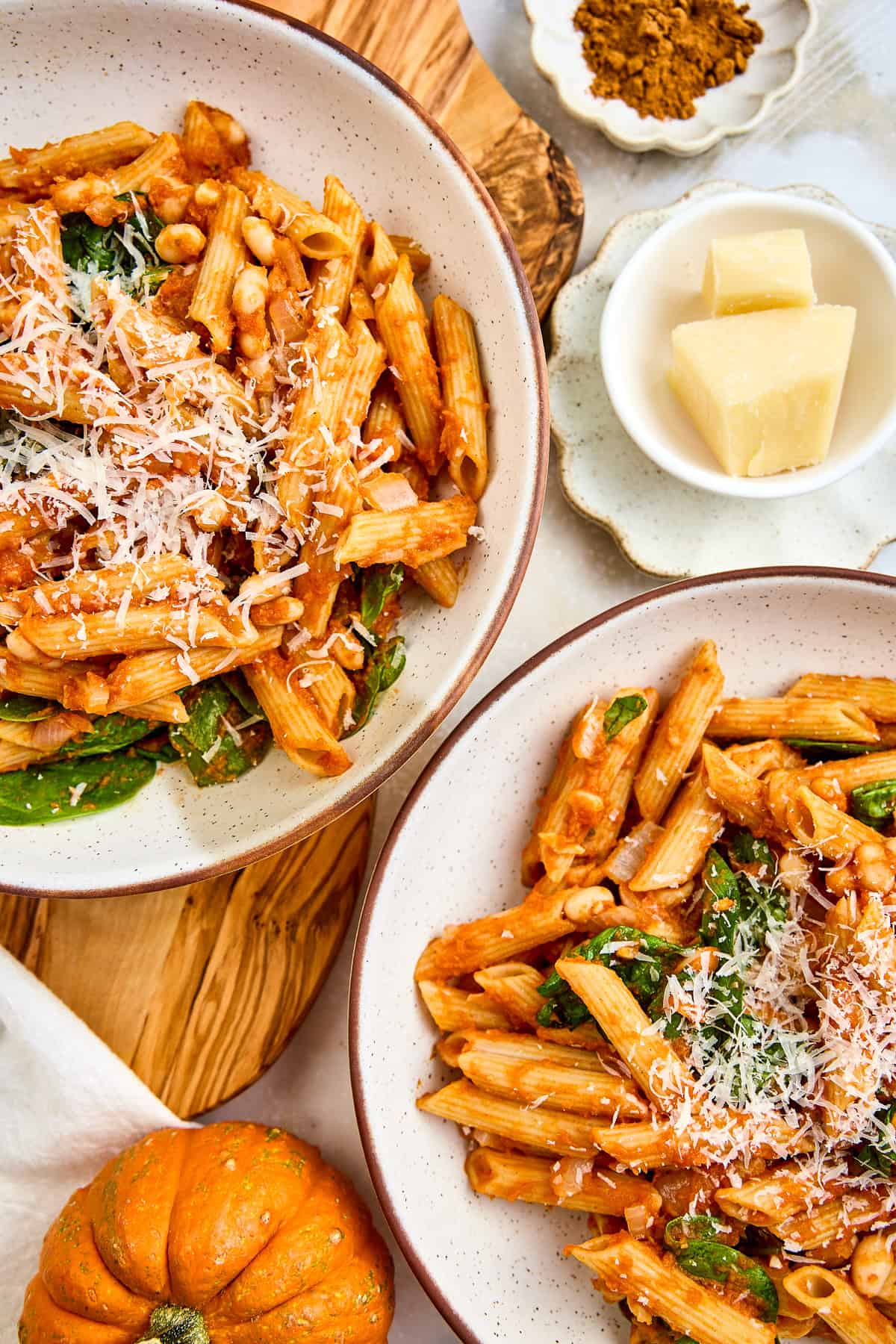 Two bowls of pumpkin pasta next to ingredients and a mini pumpkin.