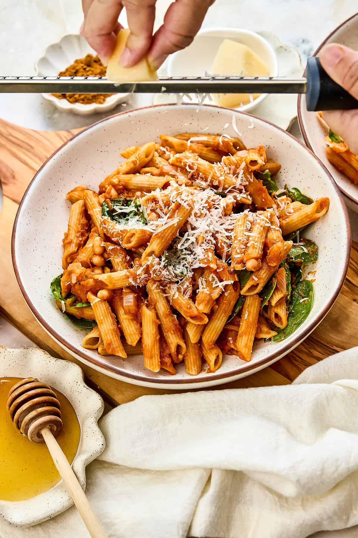 Woman grating a block of parmesan cheese over a bowl of pasta on a board.