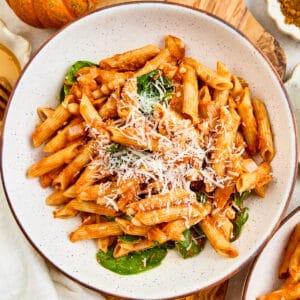 Pumpkin pasta in a bowl on a board next to a pumpkin and ingredients.