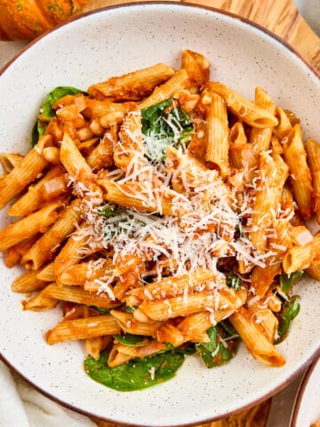 Pumpkin pasta in a bowl on a board next to a pumpkin and ingredients.