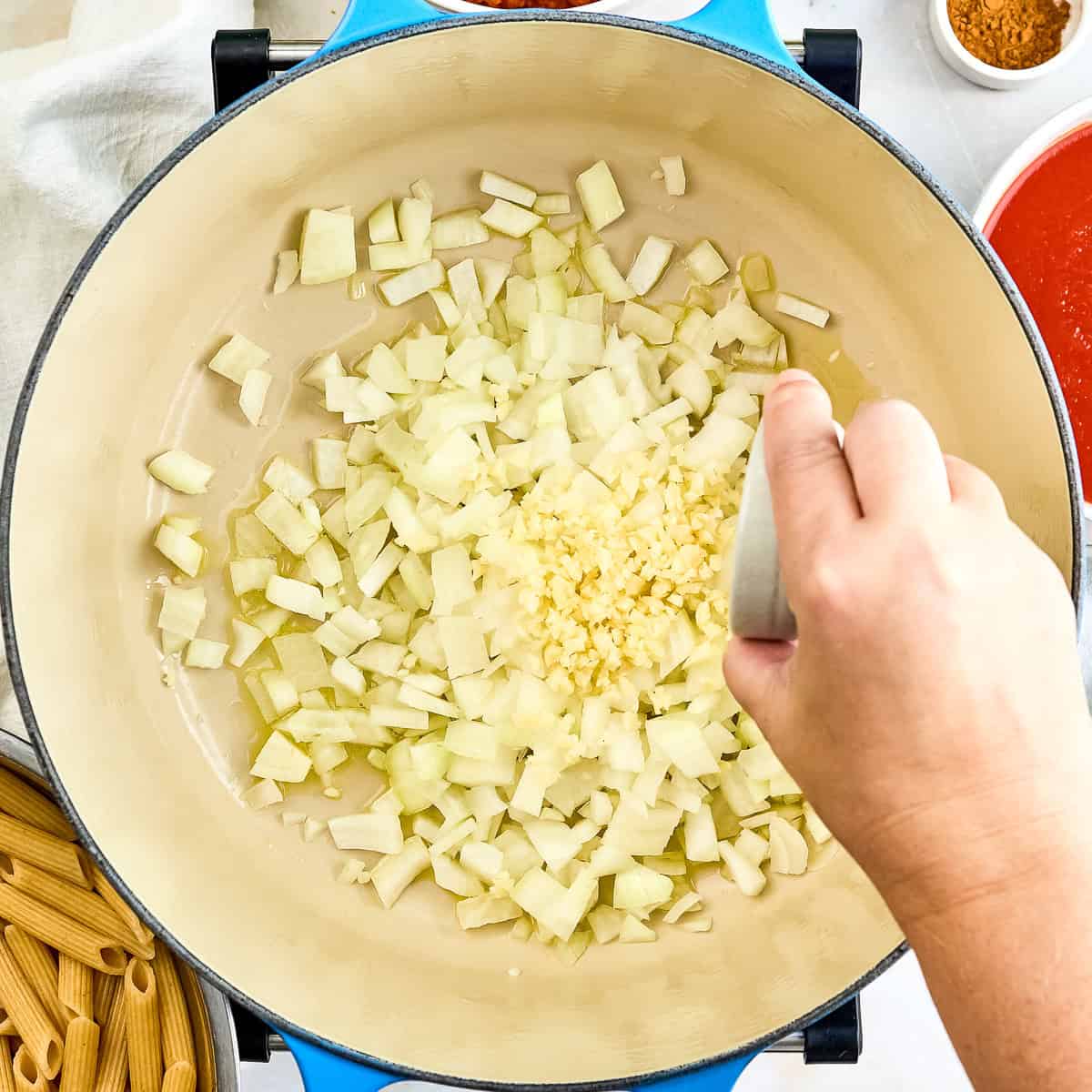 Woman adding garlic to a pot with onions cooking in olive oil.