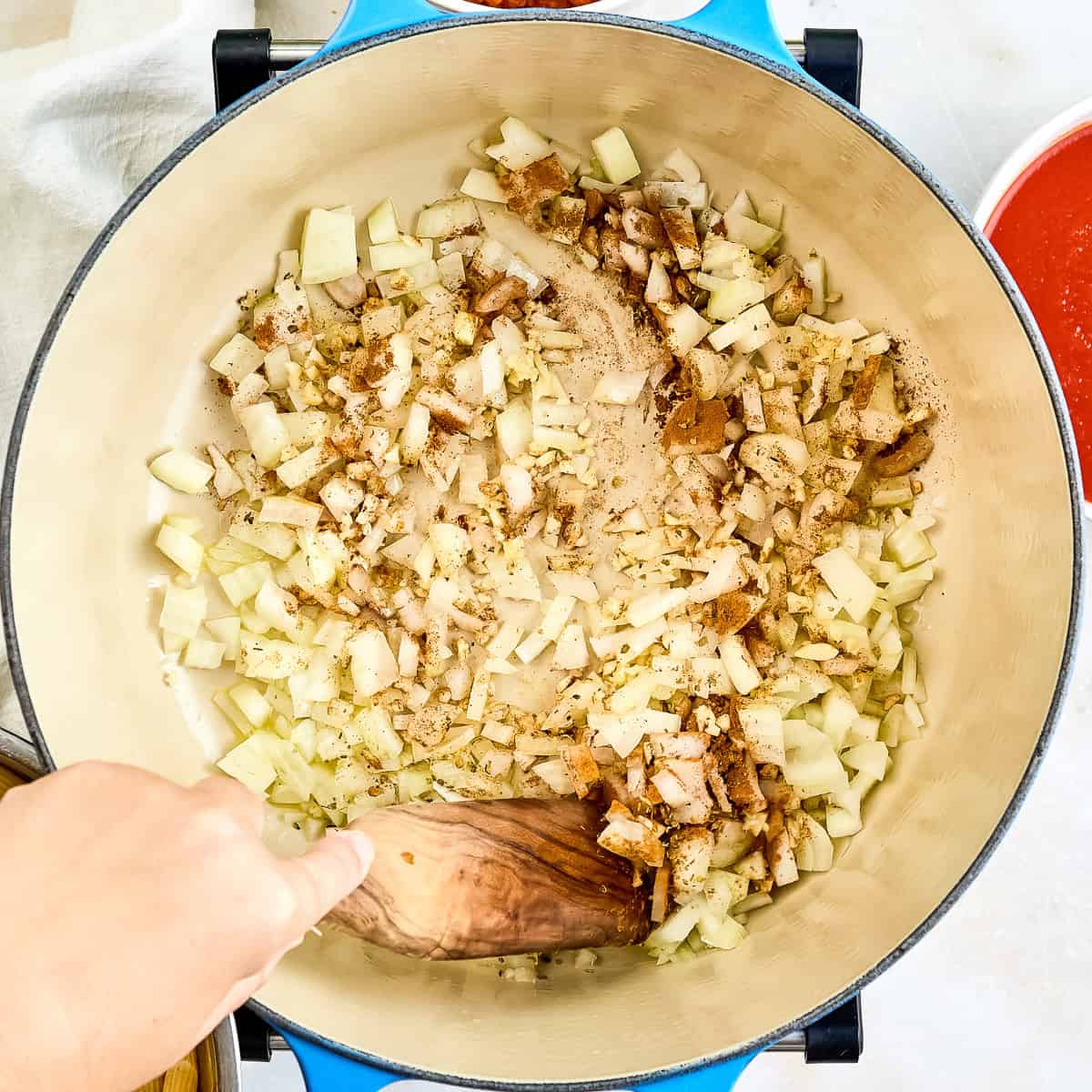 Woman stirring cinnamon, oregano, and salt into onions and garlic in a pot.