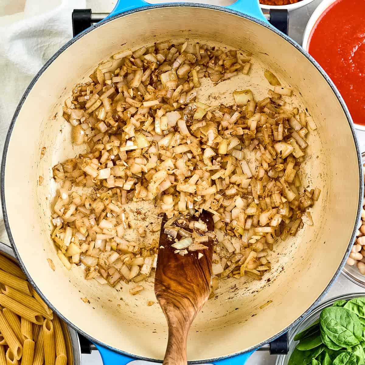 Garlic, onions, and spices cooked down in a pot with a wooden spoon.