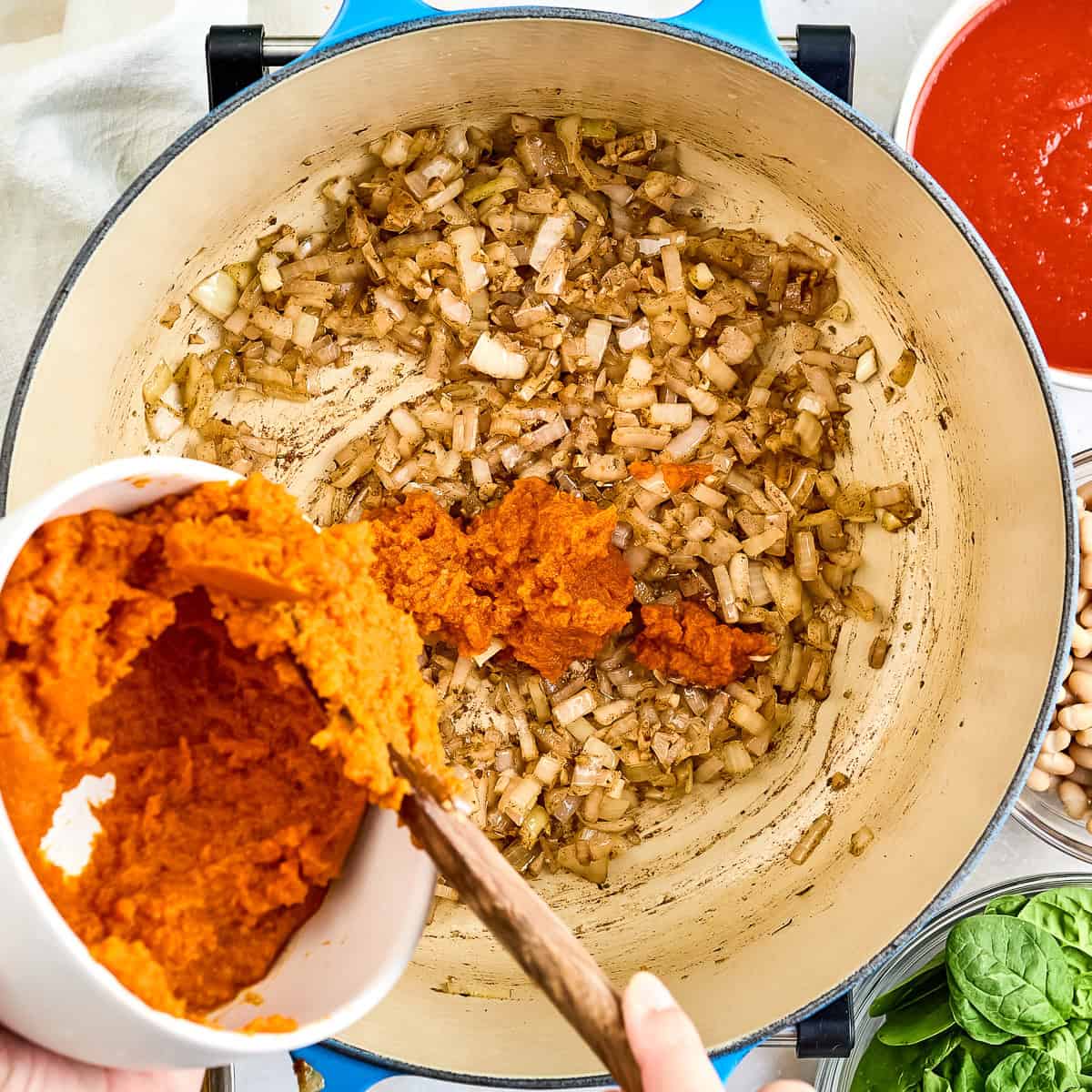 Woman adding canned pumpkin to a pot with garlic, onion, and spices.