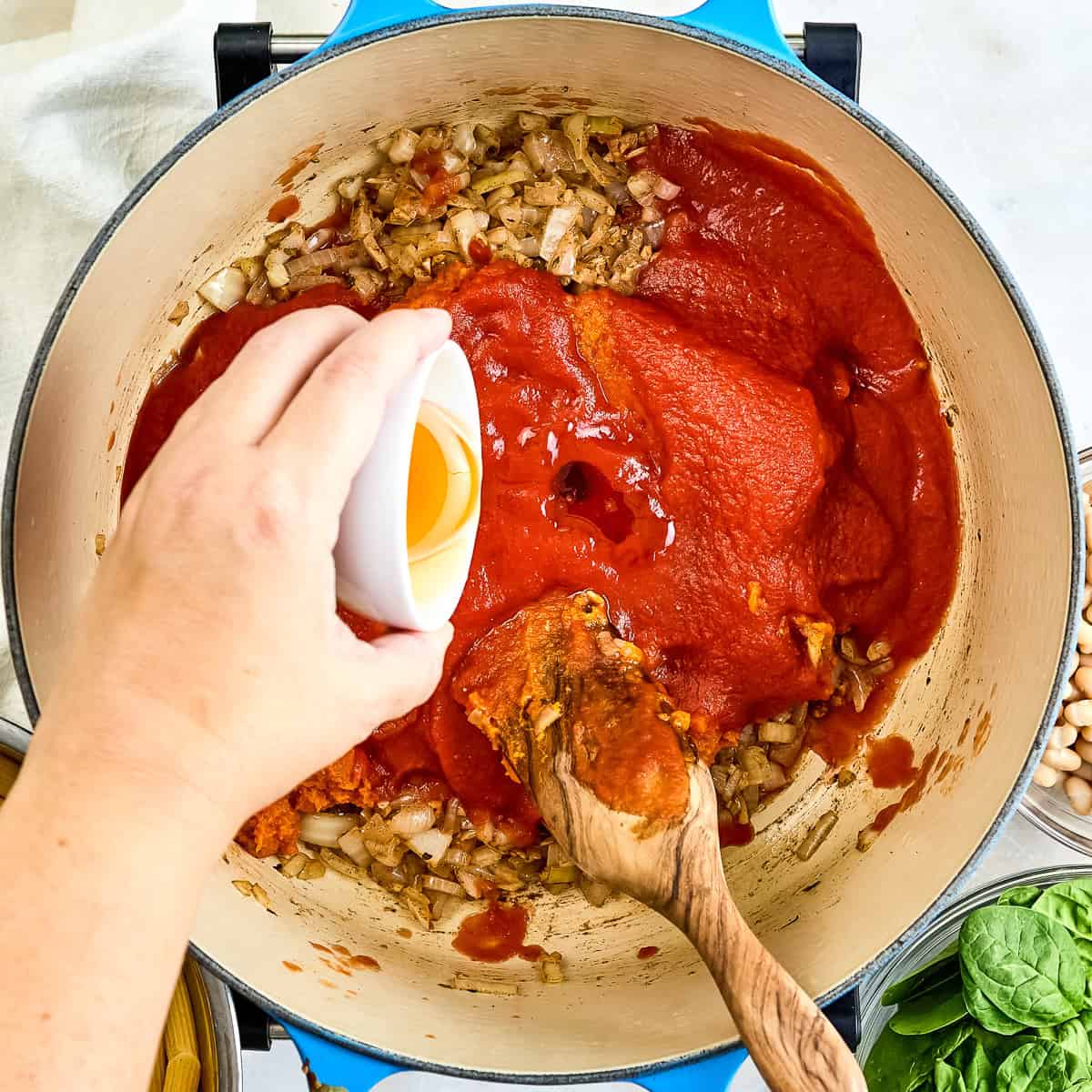 Woman adding honey to a pot with other ingredients for pumpkin pasta sauce.