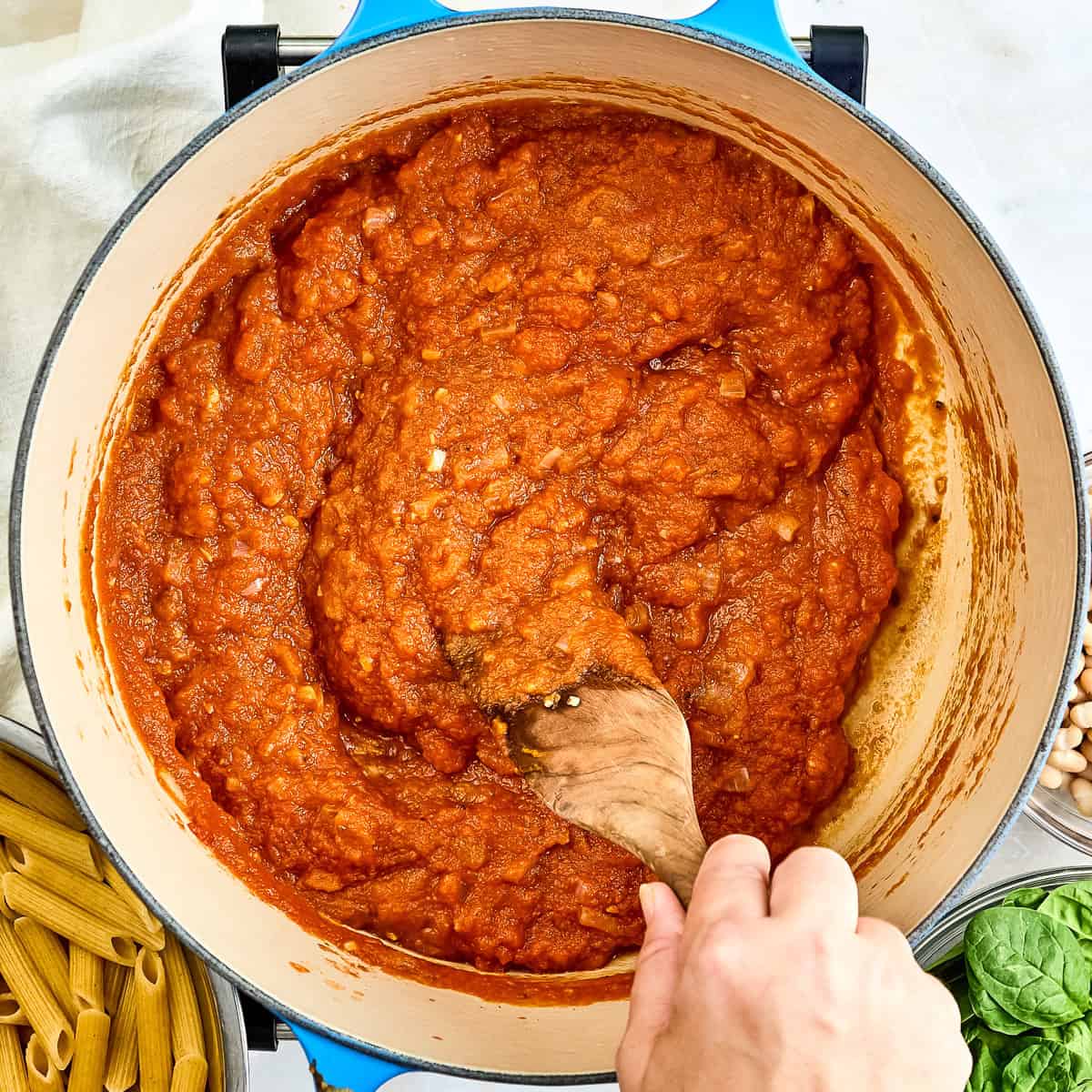 Woman stirring pumpkin pasta sauce in a pot with a wooden spoon.