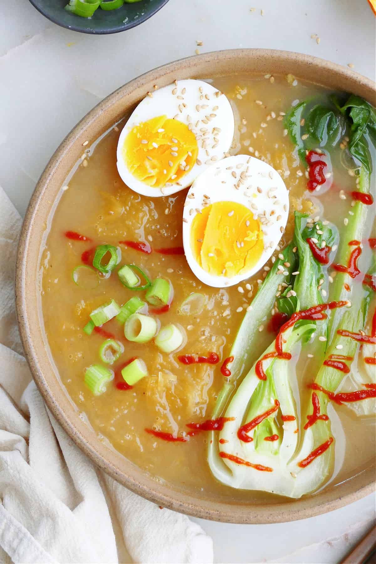 Spaghetti Squash Ramen with a boiled egg, scallions, hot sauce, and bok choy in a bowl