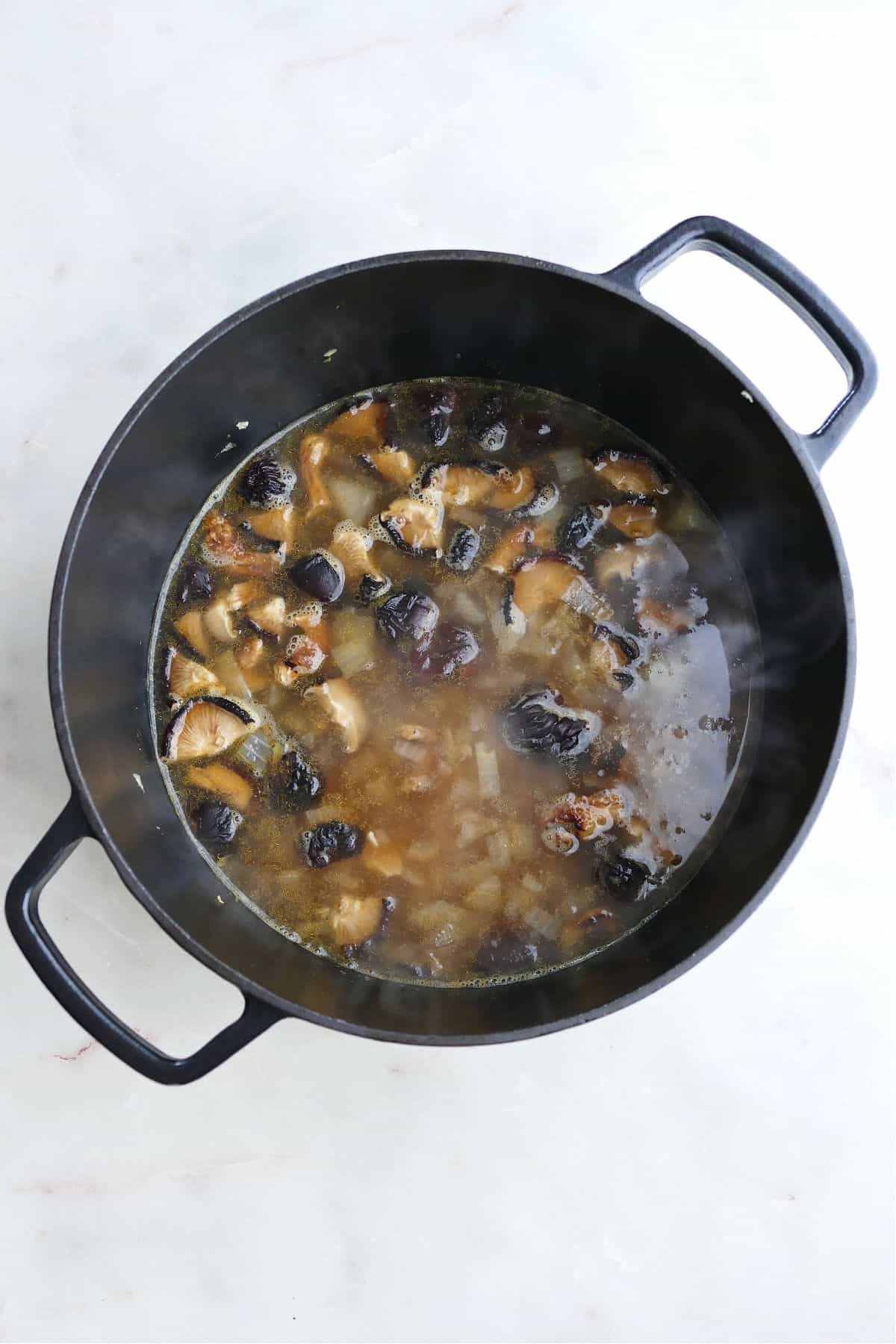 mushroom broth simmering in a large Dutch oven on a counter