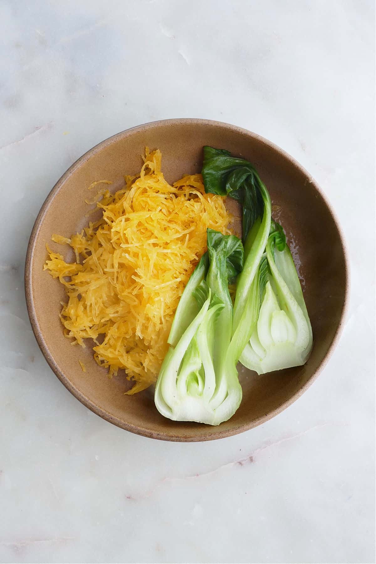 spaghetti squash noodles and bok choy in a brown serving bowl on a counter